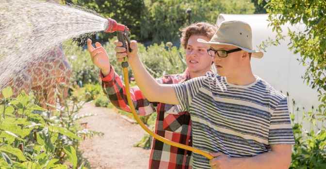 Two people standing outside, watering a garden.