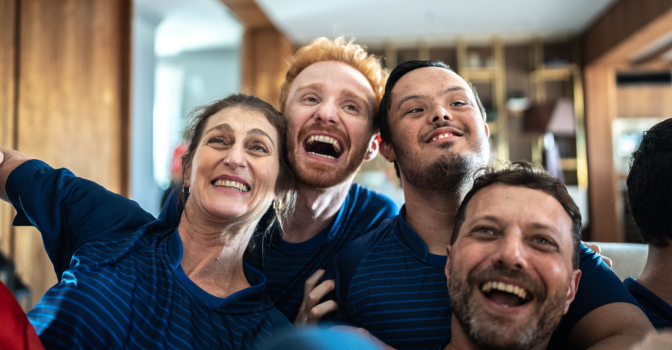 Group of 4 people, embraced with their heads together, looking forward, laughing.