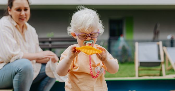 Woman sitting behind a young albino child playing in a sand pit
