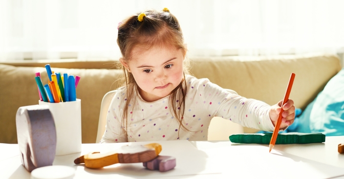 Young girl sitting at a table drawing on a piece of paper