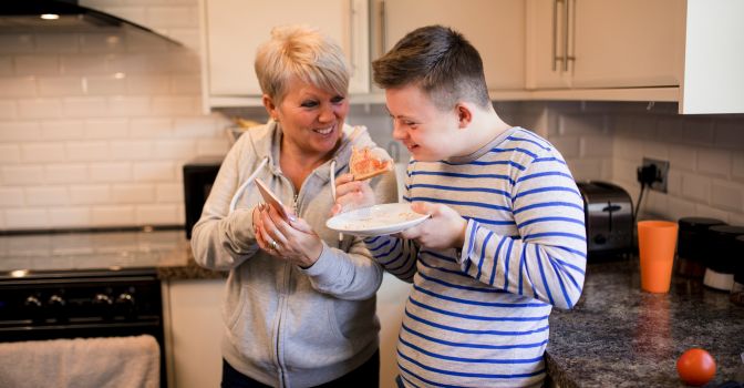 Woman showing a young man her phone while eating toast in the kitchen