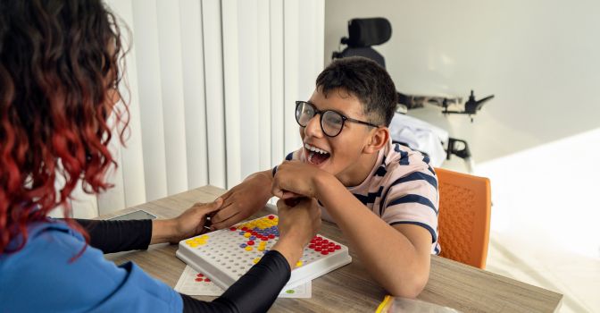 Teenage boy smiling joyously holding hands with a physical therapist